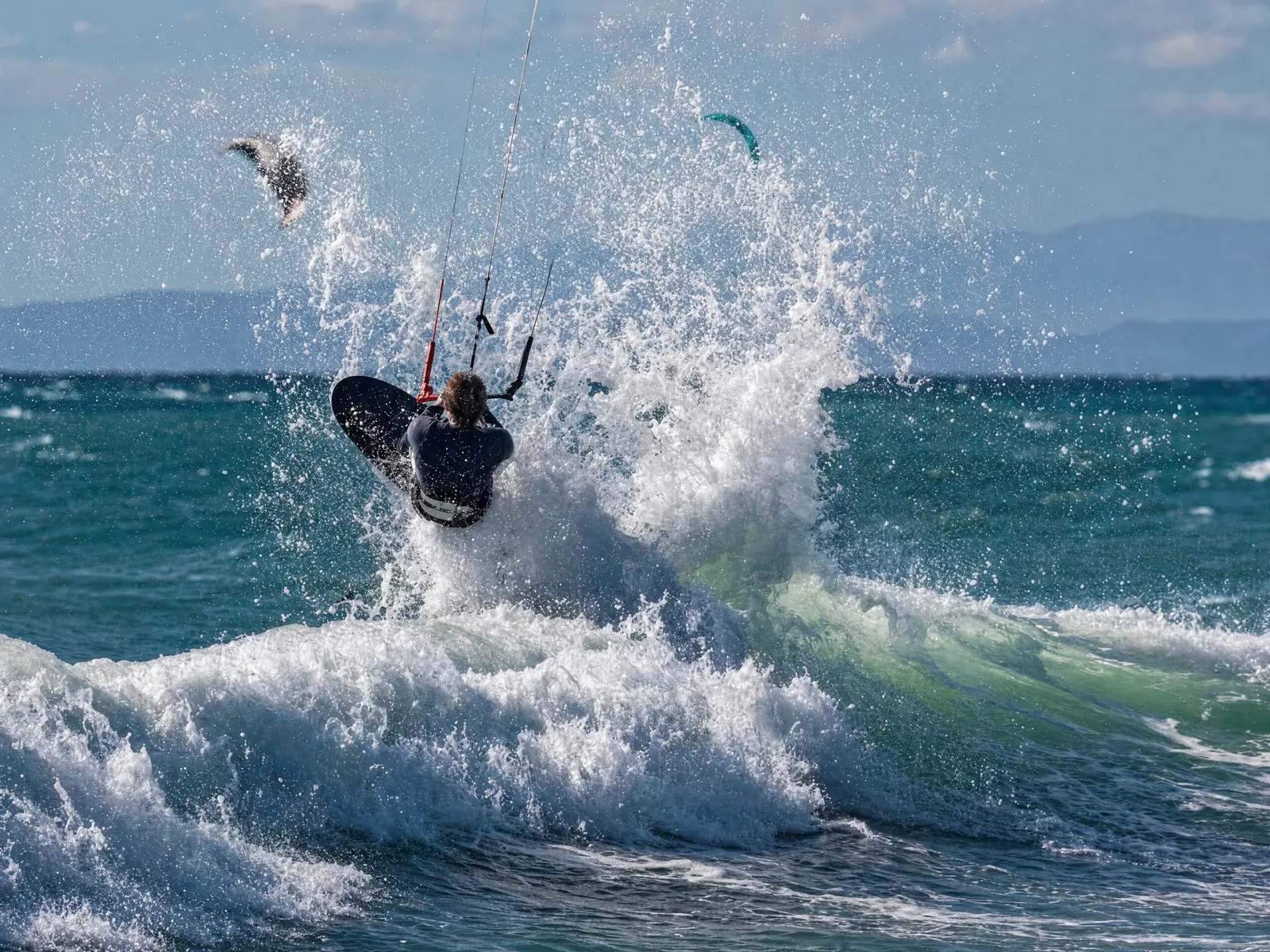 Nomad Wave Twin-Tip rider blasting a huge spray off the lip as a wave breaks, kite and board airborne behind